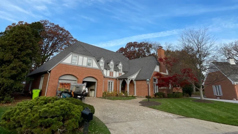 A stately brick residence featuring a charcoal slate roof finish and multiple dormers in a lush autumn setting.