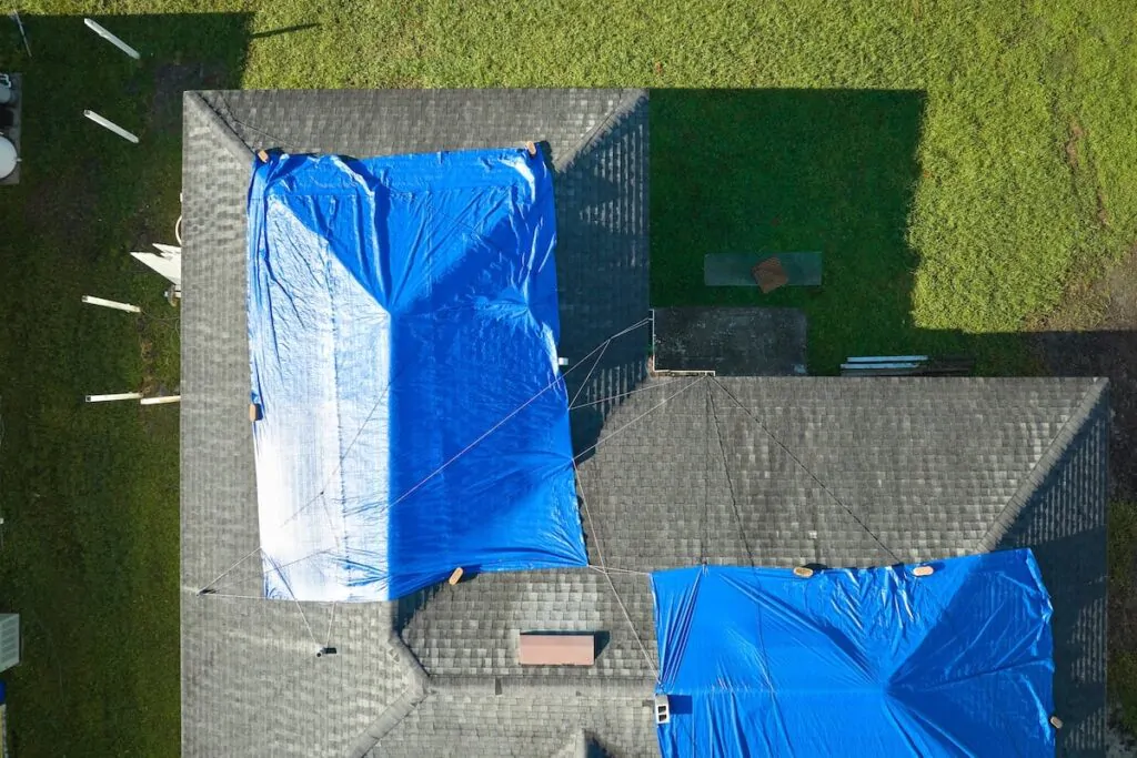 A tarp covers a significant section of the roof, representing a temporary emergency roof leak repair solution after storm damage.