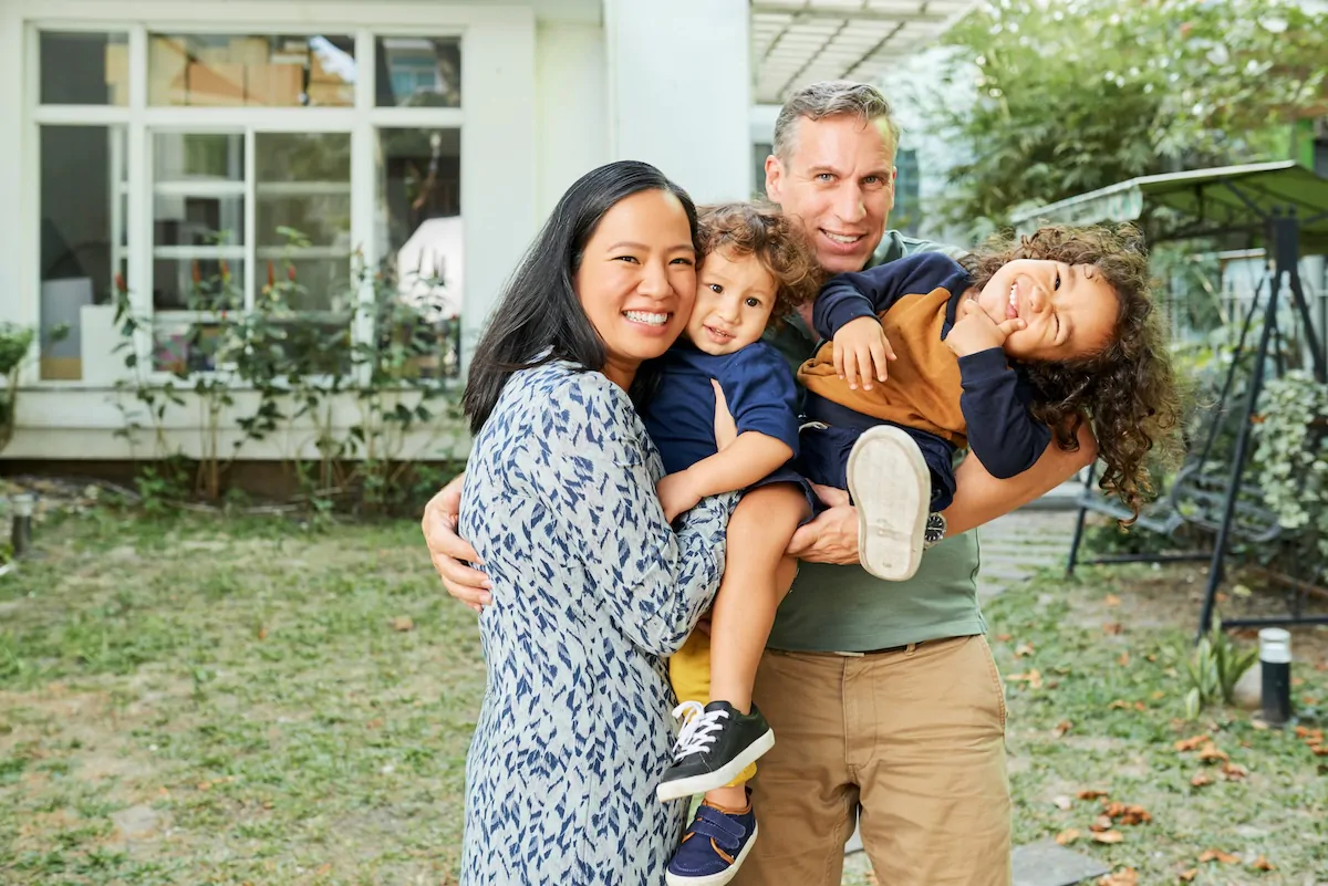 Father, mother and two kids standing in backyard of their house, smiling, laughing and looking at camera