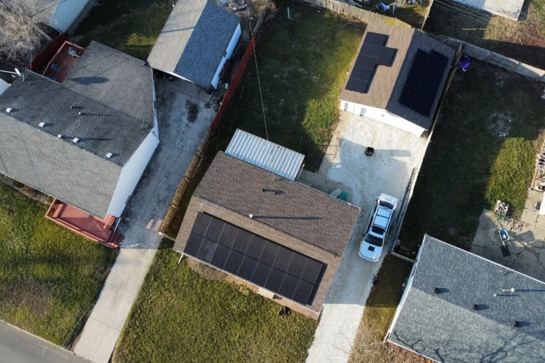 Bird's-eye view of a residential property featuring several shingles roofs with solar panels installed on both the main house and a secondary garage structure.