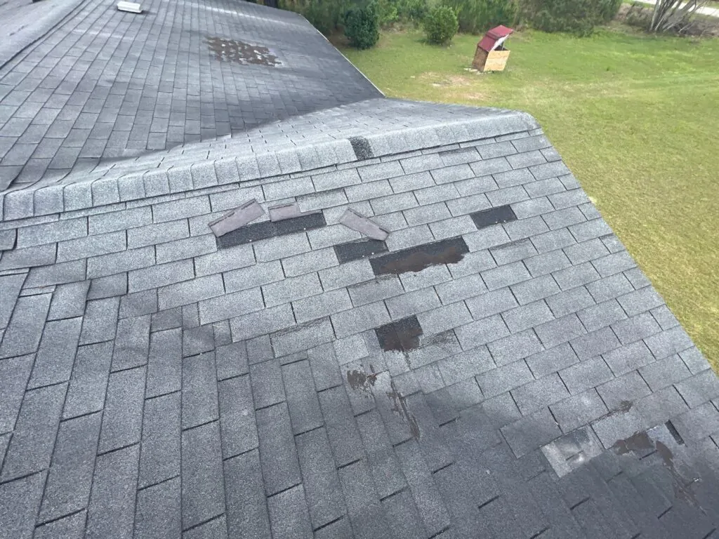 Close-up of missing and lifted asphalt shingles on a residential home requiring professional storm damage roof repair services by The Roof Tiger.