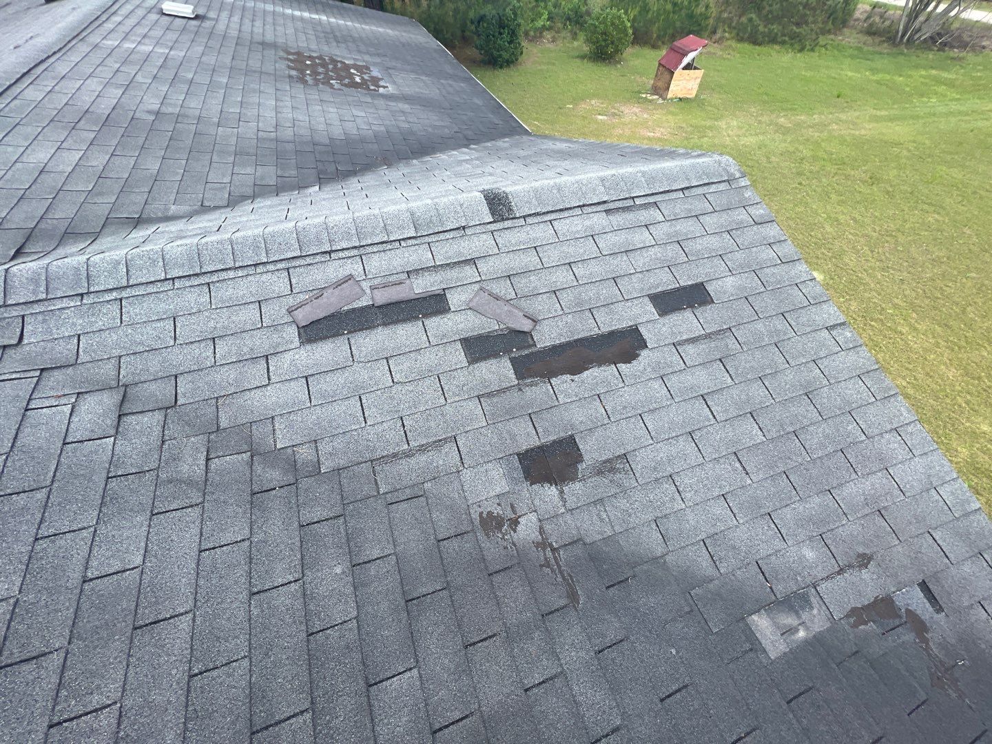 A weather-damaged roof area featuring several lifted shingles and exposed underlayment on a grey asphalt surface, illustrating the typical storm wear that requires a professional assessment. Roof Tiger is one of the top GAF roofing companies Peoria IL has to offer