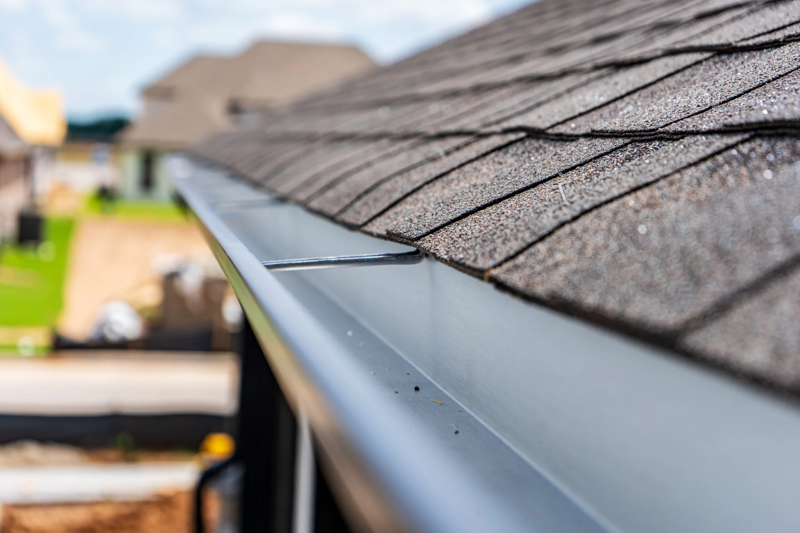 A crisp, close-up perspective of a seamless aluminum gutter installation on home shingles, highlighting the precision-fitted hidden hangers.