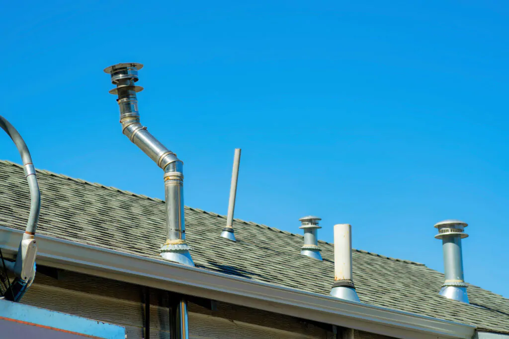 Chimney vents in rows on top of double gable style roof with gray pannels on top of house or home with gradient blue sky. Late in the afternoon sunlight in a suburban part of downtown neighborhood.