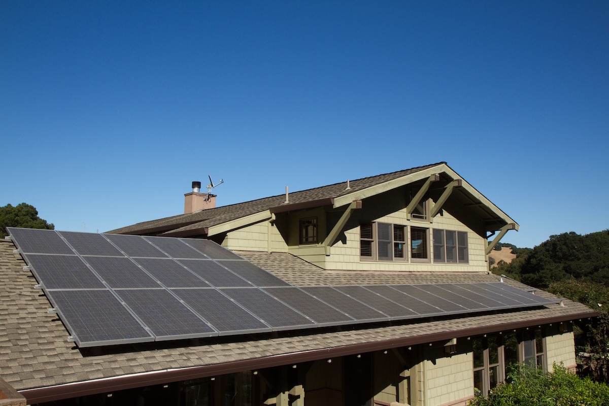 solar panels on roof of house. horizontal orientation, blue sky, gray panels on brown roof.