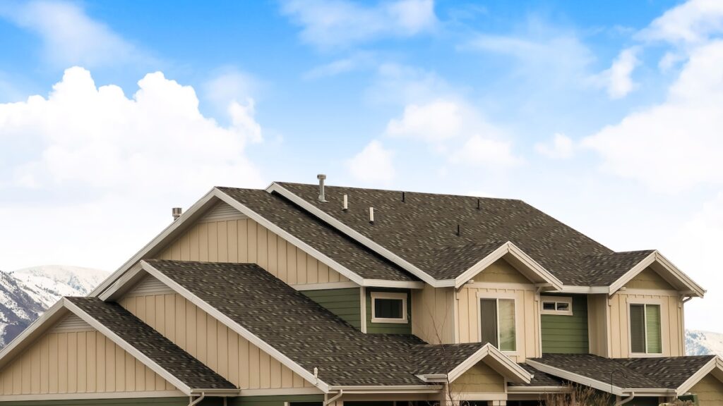 pitched roof Panorama frame House exterior with view of the dark pitched roof against a cloudy blue sky. A mountain blanketed with snow can be seen behind the home.
