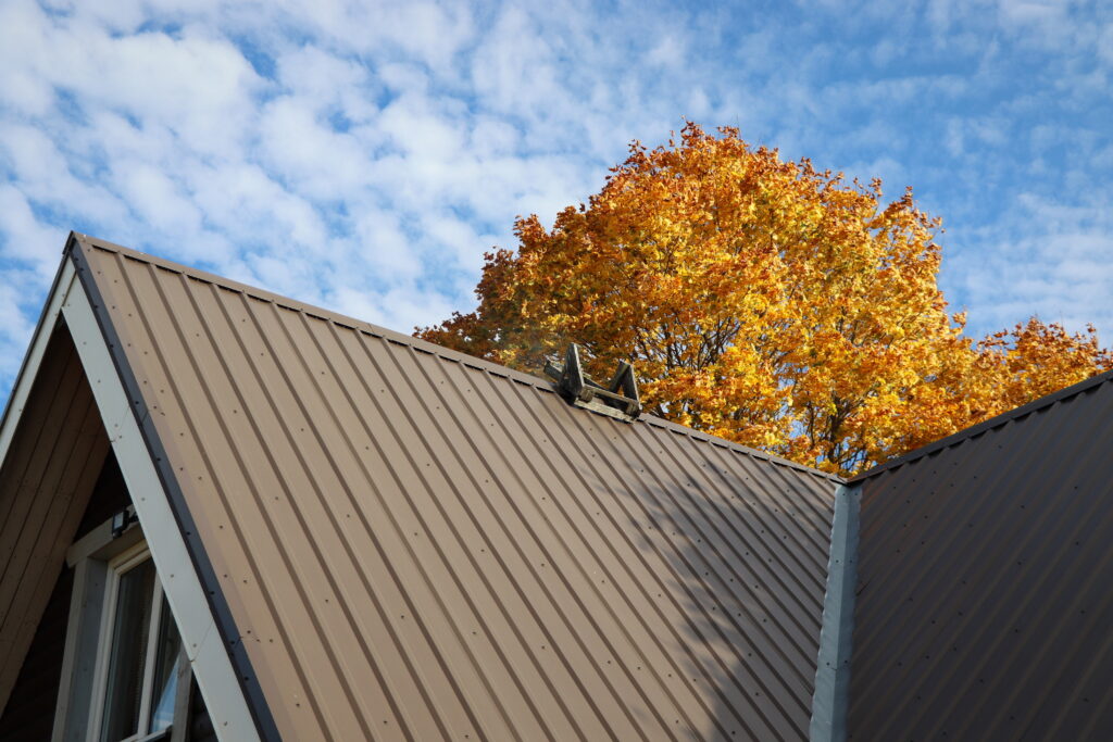 a new roofing metal roof cost Brown metalic roof house under the autmn tree against blue sky .