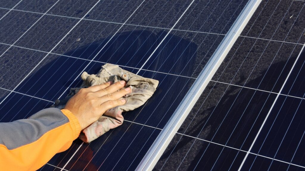 how to clean solar panels on roof Hand cleaning solar panels. A woman's hands use a towel to wipe dirty and nasty solar panels with dust and bird droppings outdoors with copy space. Selective focus