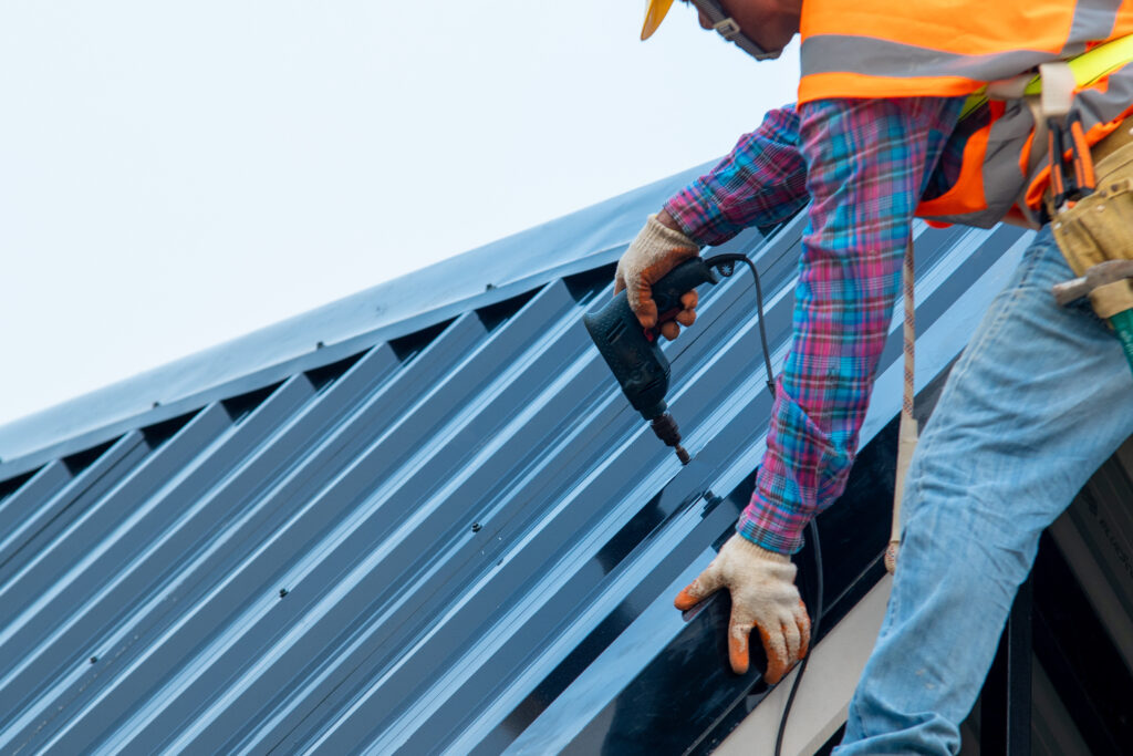 roofing companies in peoria heights Construction worker wearing safety harness belt during working on roof structure of building on construction site,Roofer using air or pneumatic nail gun and installing metal roof tile on top new roof.