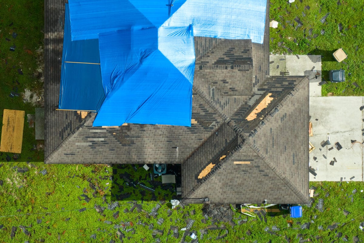Top view of a leaking house roof covered with protective tarp sheets against rainwater leaks until replacement of the asphalt shingles.