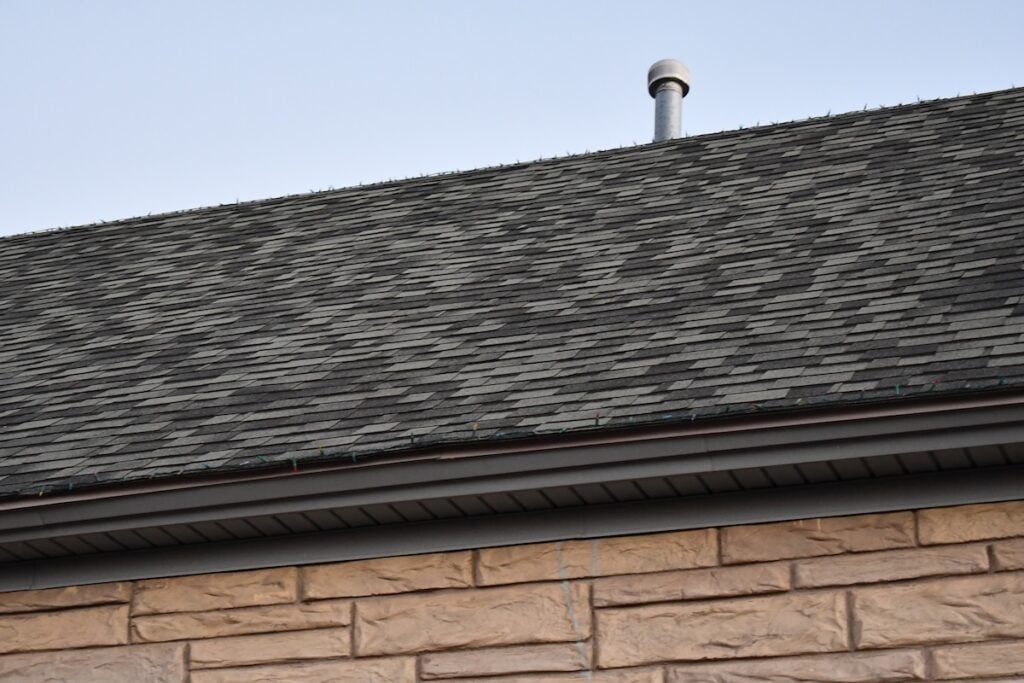 Standard 3 tab shingle roofing on classic stone structure. Small chimney vent on roof.