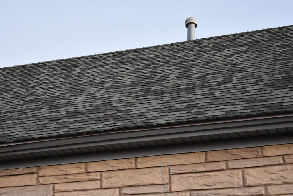 Standard 3 tab shingle roofing on classic stone structure. Small chimney vent on roof.