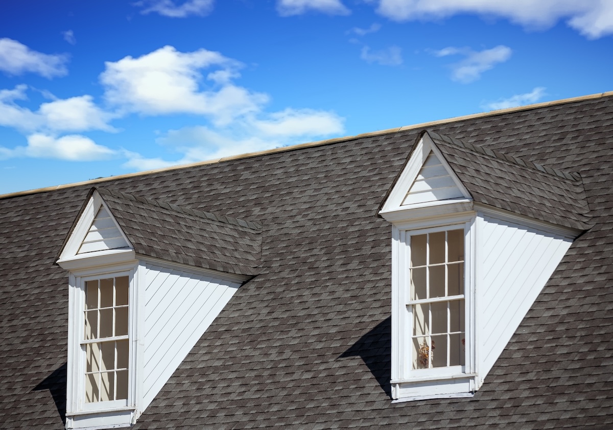 Two white wood dormers on a grey shingle roof under blue sky