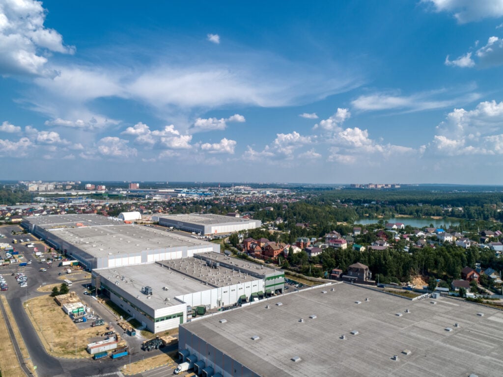 commercial roof installation Huge warehouse building with flat roof and cars on parking site under blue sky with fluffy clouds near city in summer bird eye view