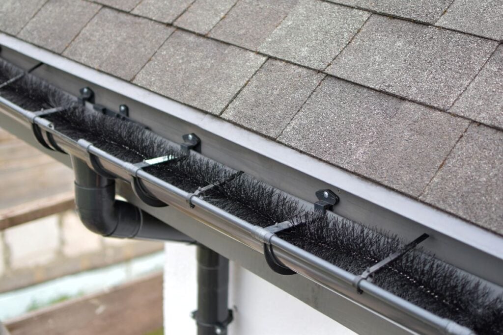 Plastic guard brush in new dark grey plastic rain gutter on asphalt shingles roof