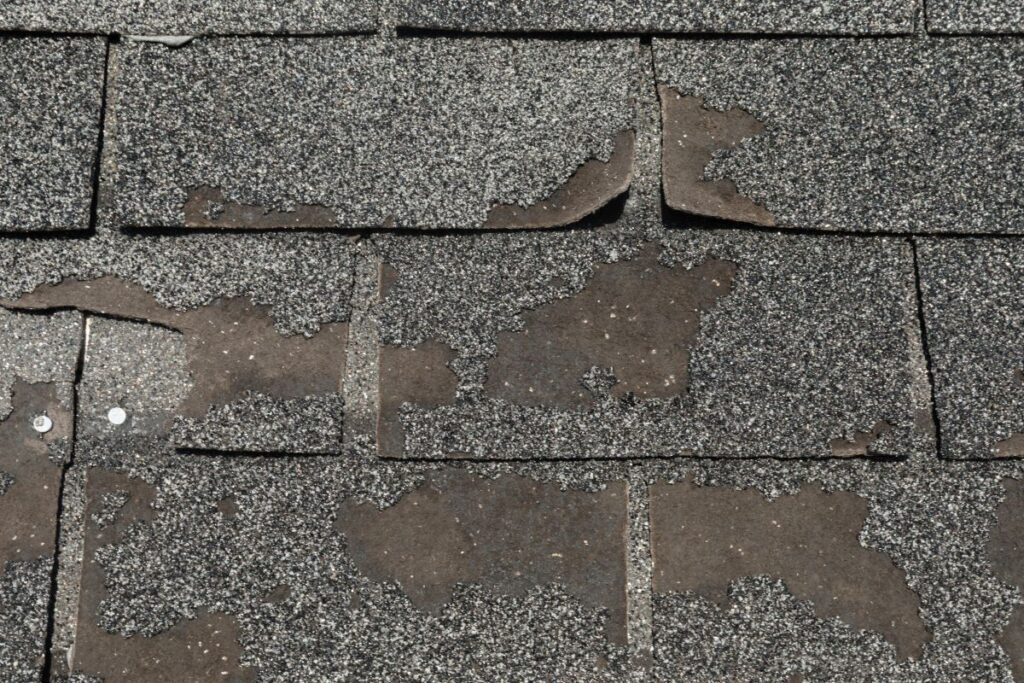 Broken and worn asphalt roofing shingles, with signs of granule loss