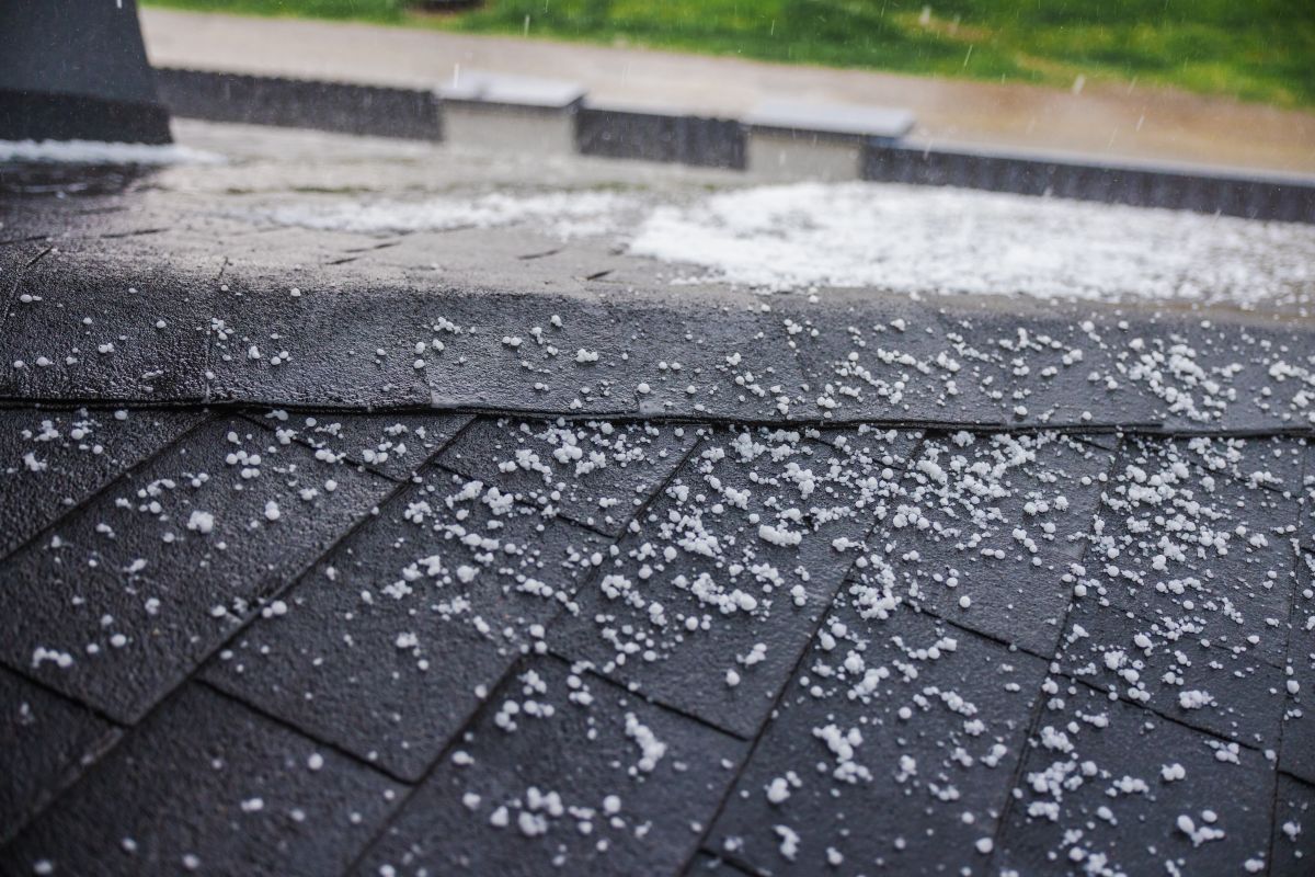 Small hailstones falling and covering a dark shingled roof during a rainstorm.